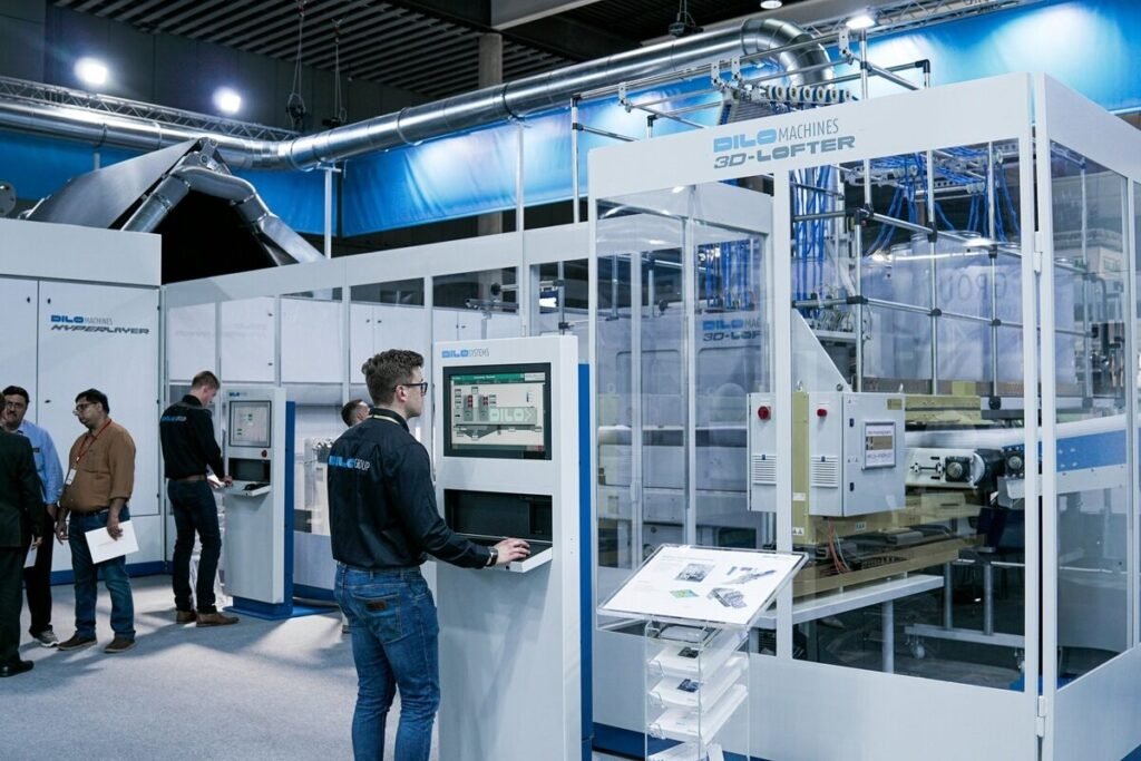 A group of people gathered around a machine in a well-lit room, engaged in discussion or observation.
