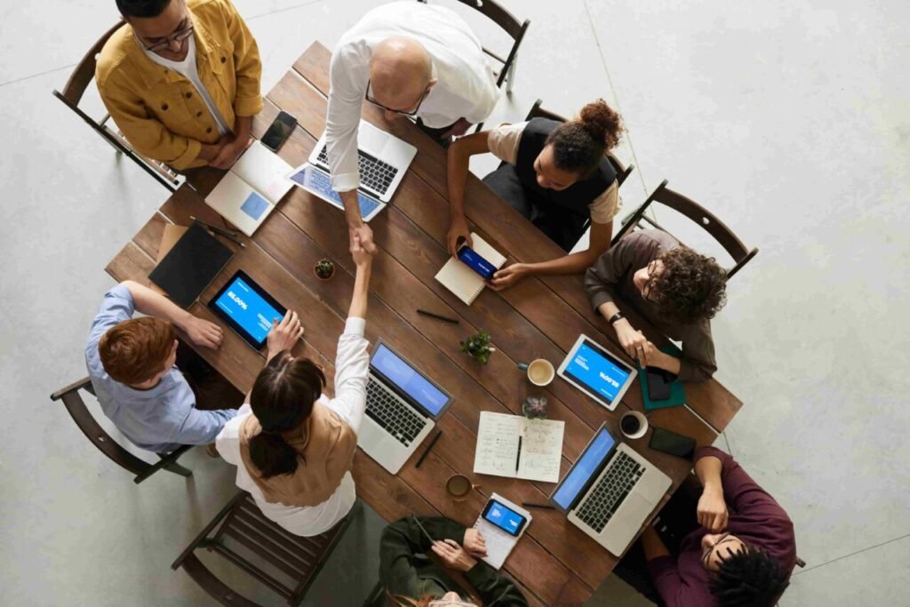 A diverse group of people seated around a table, each using laptops, engaged in discussion or collaboration.