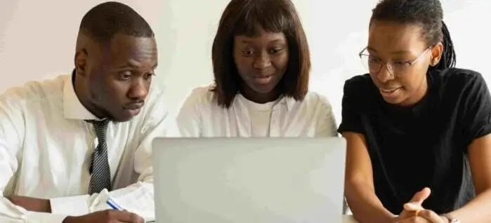 Three individuals are gathered around a laptop, intently discussing its screen content.
