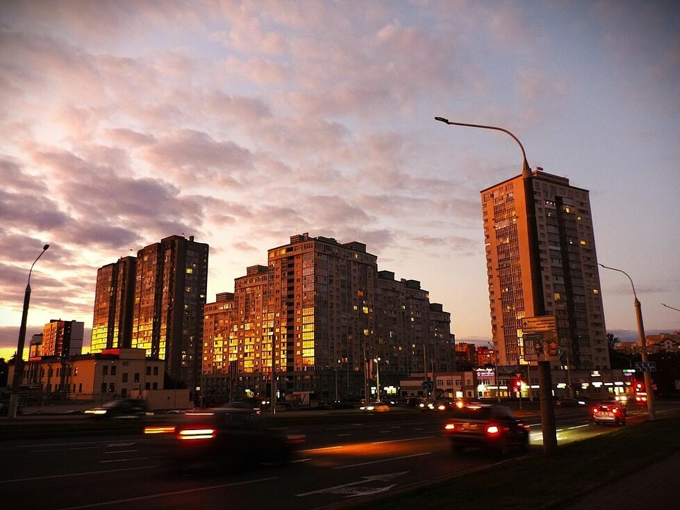 A city street at dusk, featuring cars driving by under a fading sky.